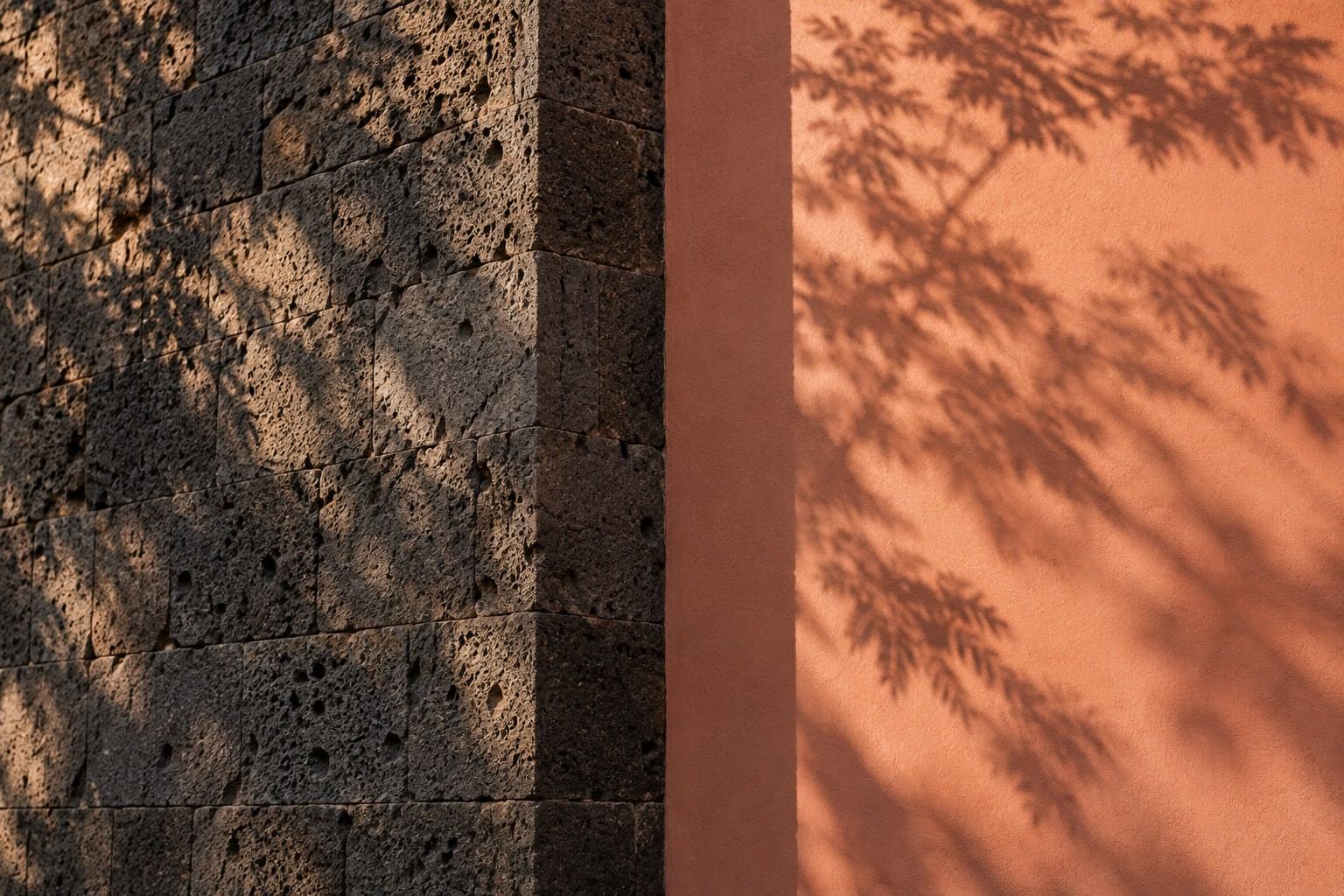 Muro de recinto volcánico junto a un muro terracota con sombras de jacaranda